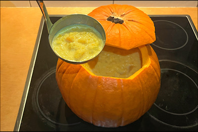 Ein Kürbis mit abgeschnittenem Deckel, aus dem eine Kürbissuppe serviert wird.